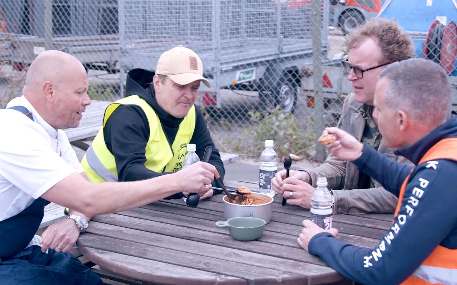 Johan, Pelle, Lennart och Kristian äter beredskapsmat ute vid en träbänk med bord.